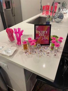 a white counter topped with lots of pink flowers and confetti sticks on top of it