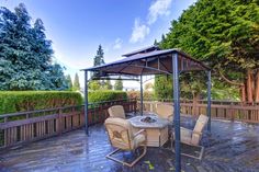 an outdoor dining table and chairs on a wooden deck with a gazebo in the background