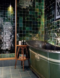 a bath tub sitting next to a wooden stool in front of a green tiled wall