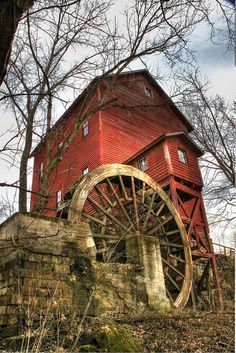 an old water wheel sits in front of a red building on the side of a hill