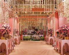 a wedding ceremony with pink and gold decorations on the wall, flowers in vases hanging from the ceiling