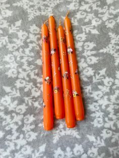 four orange candles with flowers on them sitting on a gray and white patterned tablecloth