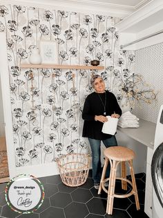 a woman standing next to a washer and dryer in a room with floral wallpaper