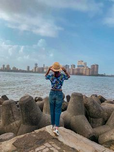 a person standing on rocks near the water with their head in his hands while looking at the city