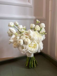 a bouquet of white flowers sitting on top of a wooden floor next to a wall