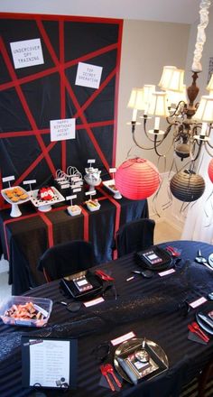 a black table topped with plates and food next to a red light bulb chandelier