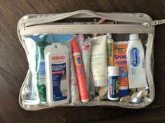 the contents of a travel bag sitting on a wooden floor, including toothbrushes and lotion