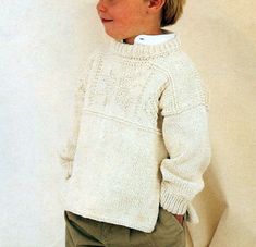 a young boy wearing a white sweater and khaki pants standing in front of a wall