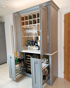 an open cabinet in the middle of a kitchen with wine glasses and bottles on it