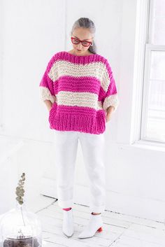 a woman standing in front of a window wearing a pink and white striped knit sweater