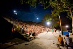 a crowd of people sitting on the steps at night with bright lights in the background