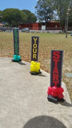 some signs that are sitting in the grass near each other on a cement slab, with one sign reading your start