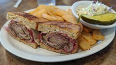 a white plate topped with a cut in half sandwich next to french fries and pickle