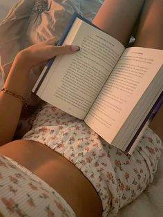 a woman laying in bed with her legs crossed and holding an open book over her stomach