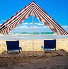 two beach chairs under an umbrella on the sand at the beach with ocean in the background