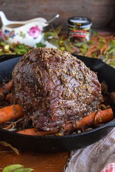 a roast beef in a cast iron skillet with carrots and herbs on the side