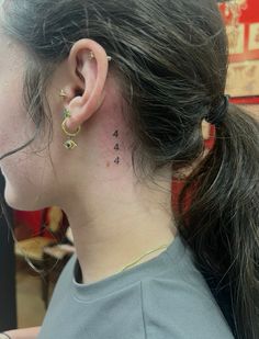 the back of a woman's neck with small tattoos on her left side ear