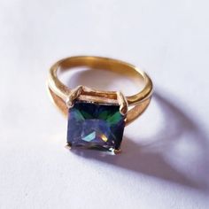 a gold ring with a blue and green stone in the center on a white surface