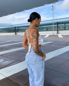 a woman with tattoos on her back standing in front of an empty parking lot at an airport