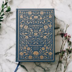 a blue book sitting on top of a white marble table next to flowers and plants