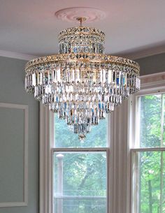 a large crystal chandelier hangs from the ceiling in front of two windows,