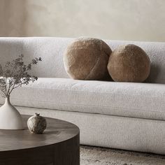 two round pillows sit on the back of a white couch next to a vase with flowers in it