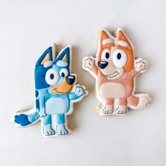 two decorated cookies sitting next to each other on a white counter top in the shape of cartoon characters