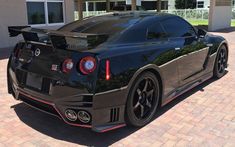 a black sports car is parked in front of a house on a brick driveway area