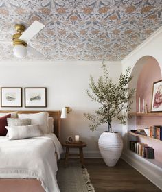 a bedroom with a bed, plant and pictures on the wall above it's headboard