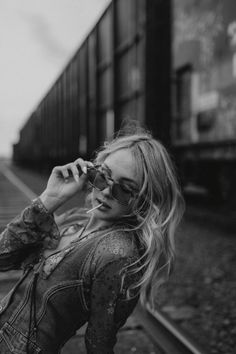 black and white photograph of woman on train tracks talking on cell phone while looking at camera