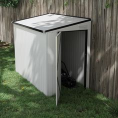 an outdoor storage shed with the door open on grass next to a fenced in yard