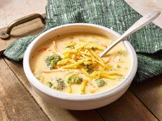 a bowl filled with broccoli cheese soup on top of a wooden table next to a green napkin