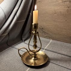 a brass candle holder with a single lit candle on top of it, next to a curtain