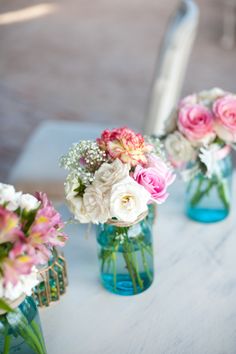 three vases filled with pink and white flowers on top of a table next to a mirror