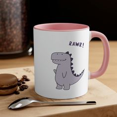 a pink and white coffee mug sitting on top of a wooden table next to a cookie