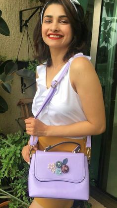 a woman holding a purple purse in front of some plants and potted planters