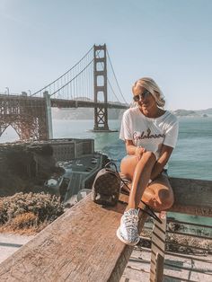 a woman sitting on top of a wooden bench in front of the golden gate bridge