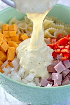 a bowl filled with pasta, ham and cheese being drizzled over it