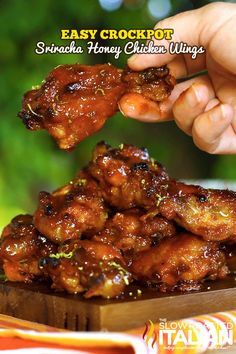 someone is picking up some chicken wings from a wooden tray