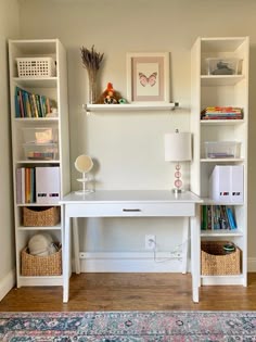 a white desk with books and baskets on it in a living room area next to a wall mounted bookcase