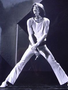 a woman in white pants standing on stage with her hands behind her back and legs crossed