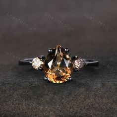 an orange diamond ring with three white diamonds on the side and black gold band, set in