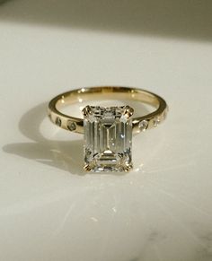 an emerald - cut diamond ring sits on a white surface