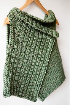 a green knitted sweater hanging on a wooden hanger next to a white wall