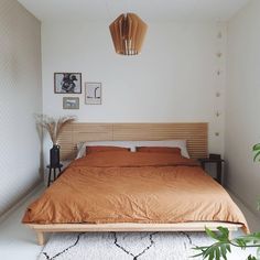 a bed with an orange comforter in a white room next to potted plants