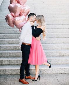 a man and woman standing next to each other on stairs with pink balloons in the air