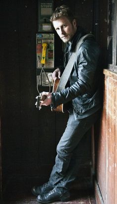 a man with a guitar leaning against a wall