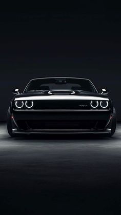 the front end of a black and white car in a dark room with its lights on