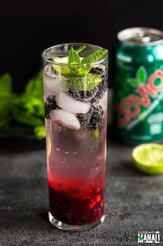 a tall glass filled with ice and blackberries on top of a table next to a can of soda