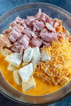 the ingredients to make cheese and ham dip in a glass bowl on a blue surface